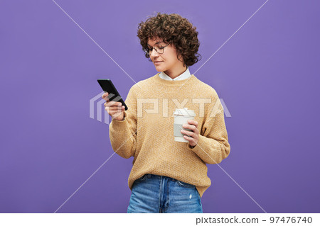 Young woman with dark short curly hair looking through photos in mobile phone 97476740