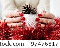 Woman's hands with red manicure and gold foil on the nails. Trendy autumn and winter nail design. Woman with a beautiful manicure holding a white knitted cup. The concept of cozy Christmas holidays. 97476817