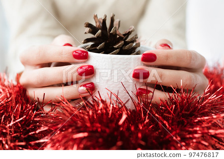 Woman's hands with red manicure and gold foil on the nails. Trendy autumn and winter nail design. Woman with a beautiful manicure holding a white knitted cup. The concept of cozy Christmas holidays. Woman's hands with red manicure and gold foil on the nails. Trendy autumn and winter nail design. Woman with a beautiful manicure holding a white knitted cup. The concept of cozy Christmas holidays. 97476817