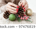 Female hands with red manicure and gold foil on the nails. Winter and Christmas time concept. Manicured woman's hands with Christmas decoration. 97476819