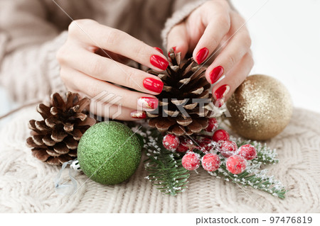 Female hands with red manicure and gold foil on the nails. Winter and Christmas time concept. Manicured woman's hands with Christmas decoration. Female hands with red manicure and gold foil on the nails. Winter and Christmas time concept. Manicured woman's hands with Christmas decoration. 97476819