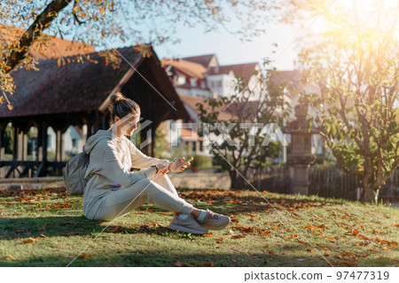 Young Fashionable Teenage Girl With Smartphone In Europian Park In Autumn Sitting At Smiling. Trendy Young Woman In Fall In Park Texting. Retouched, Vibrant Colors. Beautiful Blonde Teenage Girl Young Fashionable Teenage Girl With Smartphone In Europian Park In Autumn Sitting At Smiling. Trendy Young Woman In Fall In Park Texting. Retouched, Vibrant Colors. Beautiful Blonde Teenage Girl 97477319