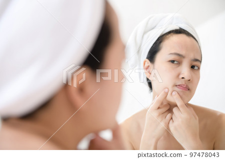 Problem skin. Concerned young asian women popping pimple on cheek while standing near mirror in bathroom. young asian women with acne Problem skin. Concerned young asian women popping pimple on cheek while standing near mirror in bathroom. young asian women with acne 97478043