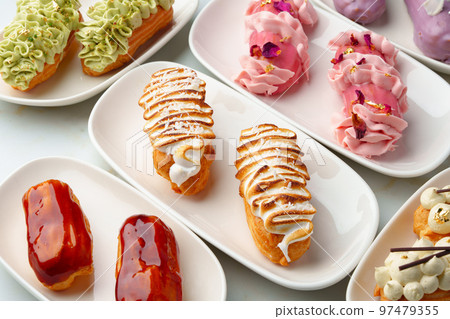 Set of colored eclairs with whipped cream on white plates 97479355