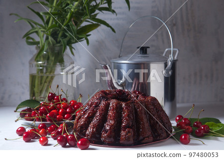 Chocolate cake with sweet cherry, vintage kettle and bouquet of blue flowers on white background.. Chocolate cake with sweet cherry, vintage kettle and bouquet of blue flowers on white background.. 97480053