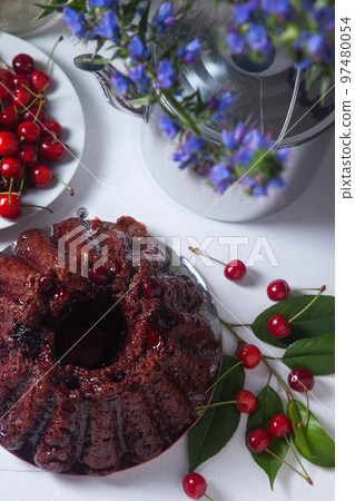 Chocolate cake with sweet cherry, vintage kettle and bouquet of blue flowers on white background.. Chocolate cake with sweet cherry, vintage kettle and bouquet of blue flowers on white background.. 97480054