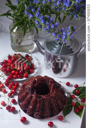 Chocolate cake with sweet cherry, vintage kettle and bouquet of blue flowers on white background.. Chocolate cake with sweet cherry, vintage kettle and bouquet of blue flowers on white background.. 97480055