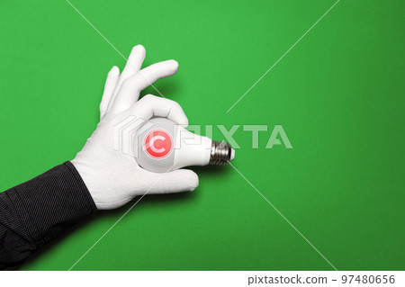 International Intellectual Property Day. A white-gloved hand holds a light bulb with an intellectual property symbol. Copy space. Green background. The concept of copyright and ideas International Intellectual Property Day. A white-gloved hand holds a light bulb with an intellectual property symbol. Copy space. Green background. The concept of copyright and ideas 97480656