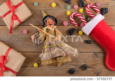The witch Befana and red stocking with sweet coal and candy on rustic wooden background. Italian Epiphany day tradition The witch Befana and red stocking with sweet coal and candy on rustic wooden background. Italian Epiphany day tradition 97480747