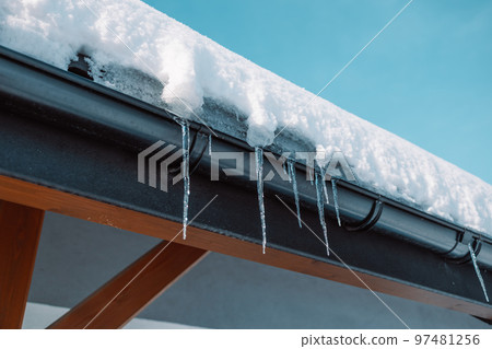 Sharp icicles and melted snow hanging from eaves of roof. Beautiful transparent icicles slowly gliding of a roof. Sharp icicles and melted snow hanging from eaves of roof. Beautiful transparent icicles slowly gliding of a roof. 97481256