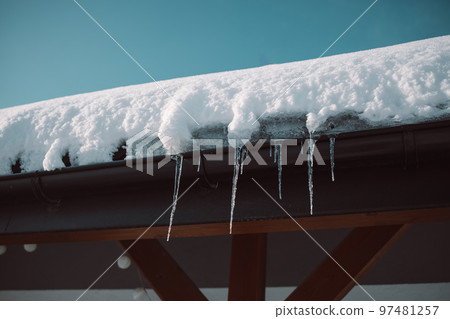 Sharp icicles and melted snow hanging from eaves of roof. Beautiful transparent icicles slowly gliding of a roof. Sharp icicles and melted snow hanging from eaves of roof. Beautiful transparent icicles slowly gliding of a roof. 97481257