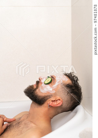 man with cucumber and face mask relaxing in bath at home 97481878