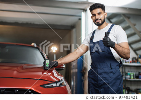 Professional service specialist testing thickness of the car paint in protective gloves. 97483421