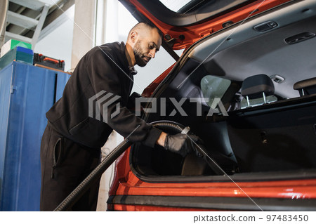 Young confident car wash service worker, doing wet cleaning of luxurious vehicle luggage trunk Young confident car wash service worker, doing wet cleaning of luxurious vehicle luggage trunk 97483450