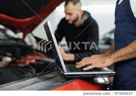 Close up view of hand of young male mechanic using laptop and his colleague with tablet 97484037