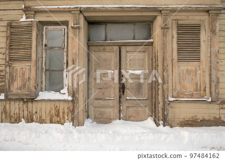 doors and windows of a very old house. snow in front of the house. winter 97484162