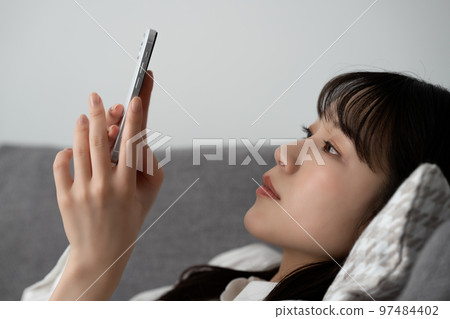 A woman lying on the sofa and using a smartphone A woman lying on the sofa and using a smartphone 97484402