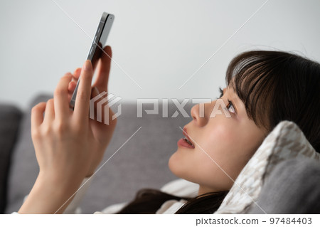 A woman lying on the sofa and using a smartphone A woman lying on the sofa and using a smartphone 97484403