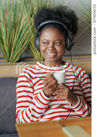 African American woman in striped sweatshirt listens to podcast with headphones. music or radio online African American woman in striped sweatshirt listens to podcast with headphones. music or radio online 97484619
