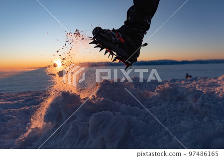 Man climbs a mountain peak in winter during sunrise. A shoe with spikes on - crampons.  97486165