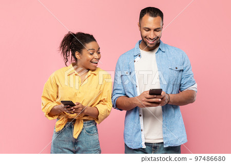 Curious black woman trying to look at her boyfriend's cellphone, man using his gadget and chatting, pink background Curious black woman trying to look at her boyfriend's cellphone, man using his gadget and chatting, pink background 97486680