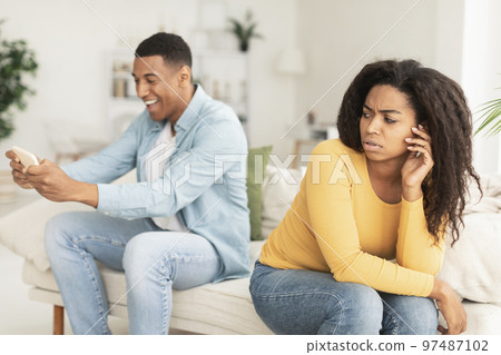 Sad young black wife look at husband, playing online game, chatting in social networks on smartphone 97487102