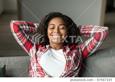 Portrait of satisfied happy millennial black lady with closed eyes relaxing on sofa, enjoying free time 97487105