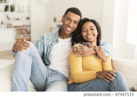 Cheerful handsome young african american man hugging his wife, resting on sofa, enjoy weekend Cheerful handsome young african american man hugging his wife, resting on sofa, enjoy weekend 97487133