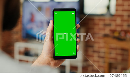Office worker working with greenscreen template on mobile phone, using smartphone with blank background and chroma key display. Looking at isolated mock up copy space. Close up. 97489463