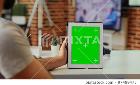 Employee analyzing greenscreen on modern tablet at home, holding digital device with isolated chroma key copyspace template. Looking at blank mockup background on portable gadget. 97489473