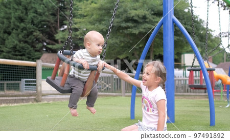Funny Little Preschool Chubby Girl Older Sister Rides Younger Newborn Infant Brother Boy On Swing. Baby Playing On Playground. Kids Entertainment, Childhood, Child Development, Happy Family Concept Funny Little Preschool Chubby Girl Older Sister Rides Younger Newborn Infant Brother Boy On Swing. Baby Playing On Playground. Kids Entertainment, Childhood, Child Development, Happy Family Concept 97491892