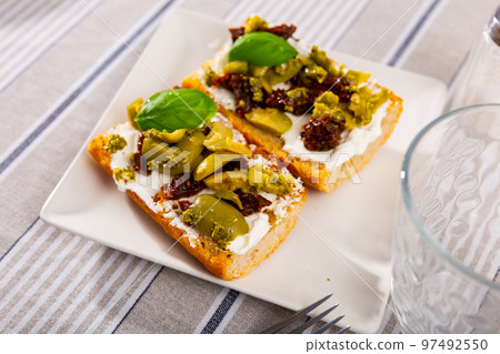 Slices of toasted bread with cream cheese, pickled olives and sun-dried tomatoes Slices of toasted bread with cream cheese, pickled olives and sun-dried tomatoes 97492550