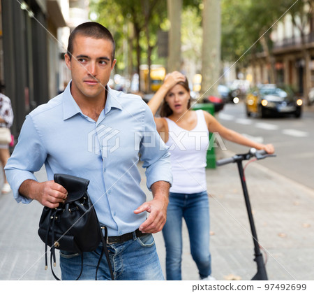 Thief stealing bag from woman riding scooter 97492699