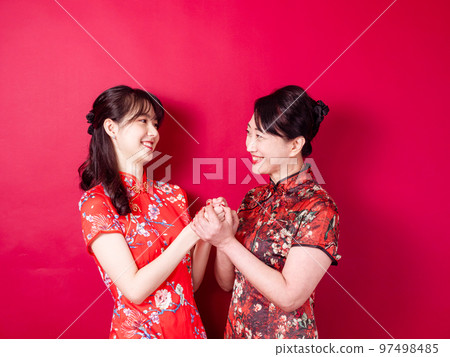 身穿紅色背景傳統旗袍的微笑的小女兒和母親的畫像。 97498485