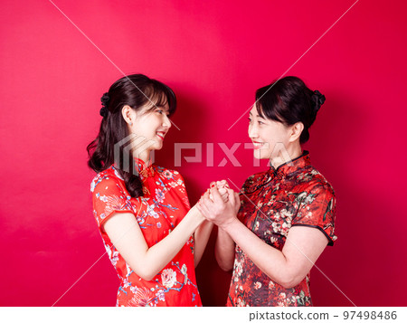 身穿紅色背景傳統旗袍的微笑的小女兒和母親的畫像。 97498486