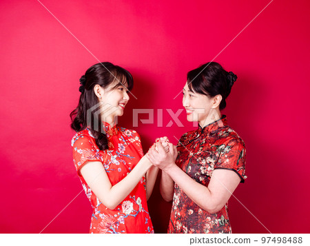 身穿紅色背景傳統旗袍的微笑的小女兒和母親的畫像。 97498488