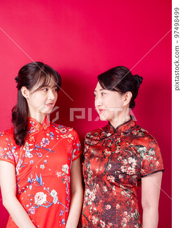 身穿紅色背景傳統旗袍的微笑的小女兒和母親的畫像。 97498499