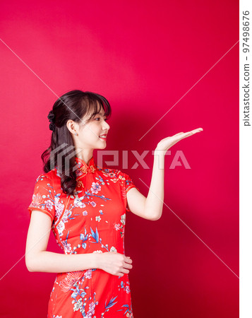 身穿傳統旗袍的亞洲年輕女性，在紅色背景中以介紹的姿態孤立。 97498676