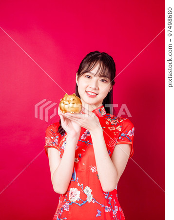 Portrait of a young Asian woman in traditional Chinese dress holding a golden piggy bank on a red background. Portrait of a young Asian woman in traditional Chinese dress holding a golden piggy bank on a red background. 97498680