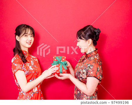 A young daughter wearing a traditional Chinese dress congratulates her mother and gives her a gift 97499196