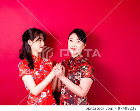 Portrait of smiling young daughter and mother wearing traditional cheongsam on red background. Portrait of smiling young daughter and mother wearing traditional cheongsam on red background. 97499232