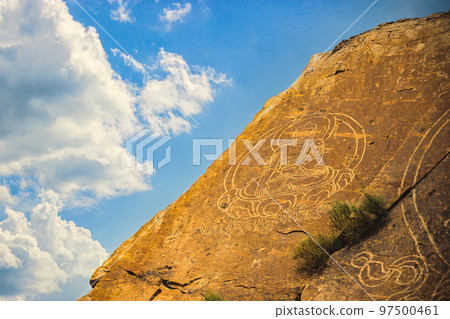 An ancient Buddha image on a stone rock against a sky with clouds 97500461
