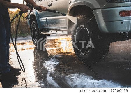 A man washes his SUV at a self-service car wash with a high-pressure water jet after off-road driving 97500469