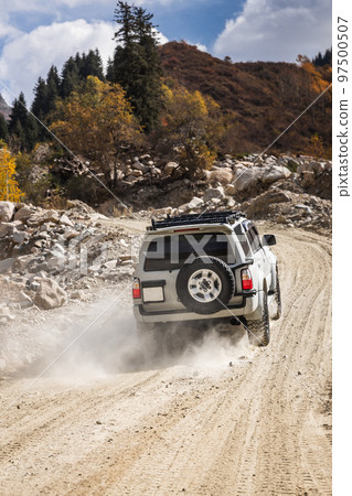 White SUV climbs a dusty road in the autumn highland, vertical White SUV climbs a dusty road in the autumn highland, vertical 97500507