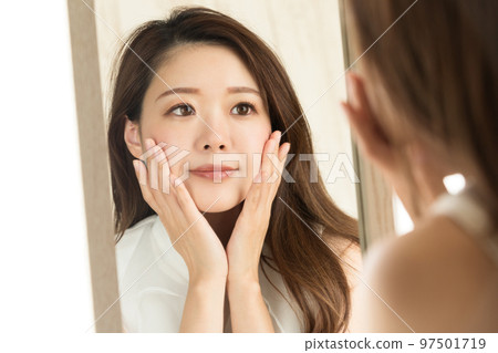 一個女人照鏡子時正在做皮膚護理。 97501719