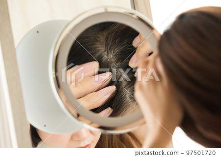 A woman looking at her scalp in the mirror. 97501720