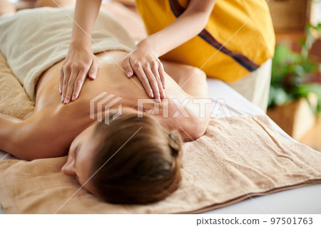 Hands of masseuse spreading oil on back of client 97501763