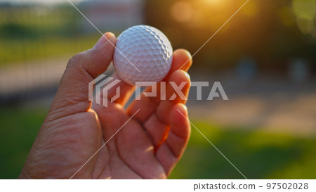 Hand hold golf ball with tee on course, golf course background 97502028