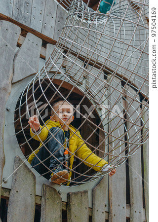 A child climbs up an alpine grid in a park on a playground on a hot summer day. children's playground in a public park, entertainment and recreation for children, mountaineering training. Child A child climbs up an alpine grid in a park on a playground on a hot summer day. children's playground in a public park, entertainment and recreation for children, mountaineering training. Child 97504169