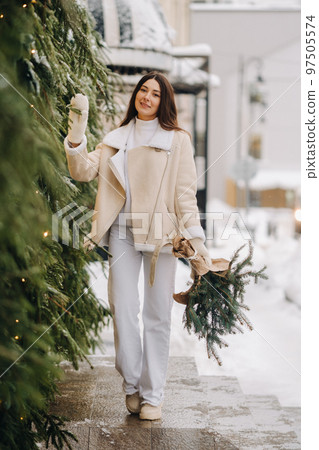 A girl with long hair in winter on the street with a bouquet of fresh fir branches A girl with long hair in winter on the street with a bouquet of fresh fir branches 97505574